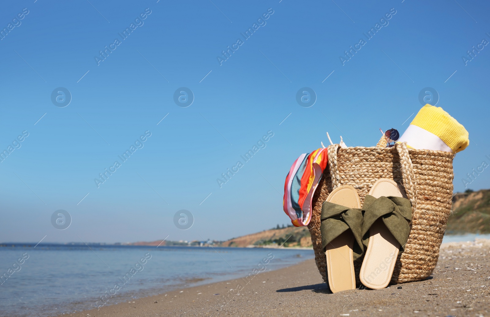 Photo of Bag with beach accessories and slippers on seaside. Space for text