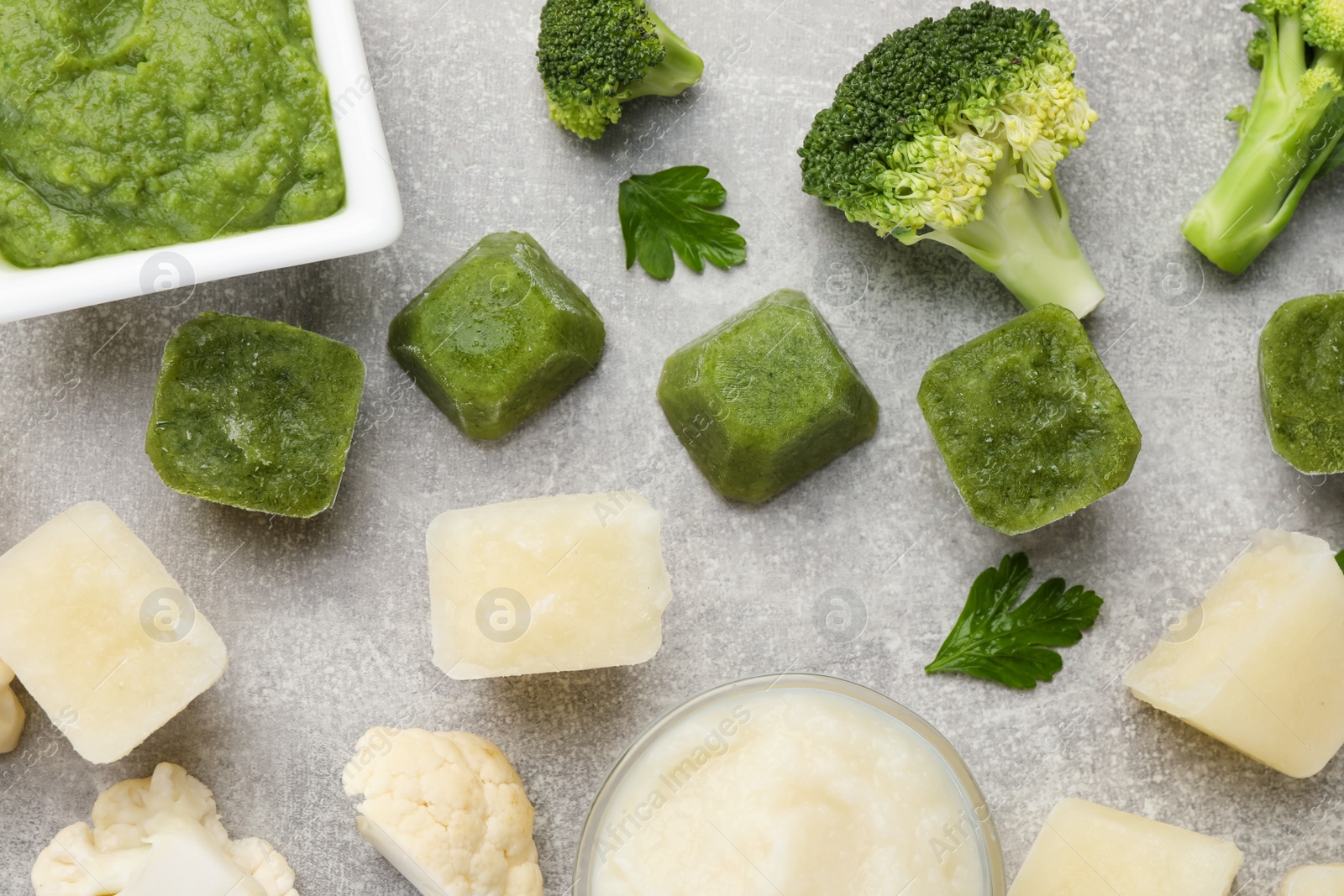 Photo of Frozen cauliflower and broccoli puree cubes with ingredients on light grey table, flat lay