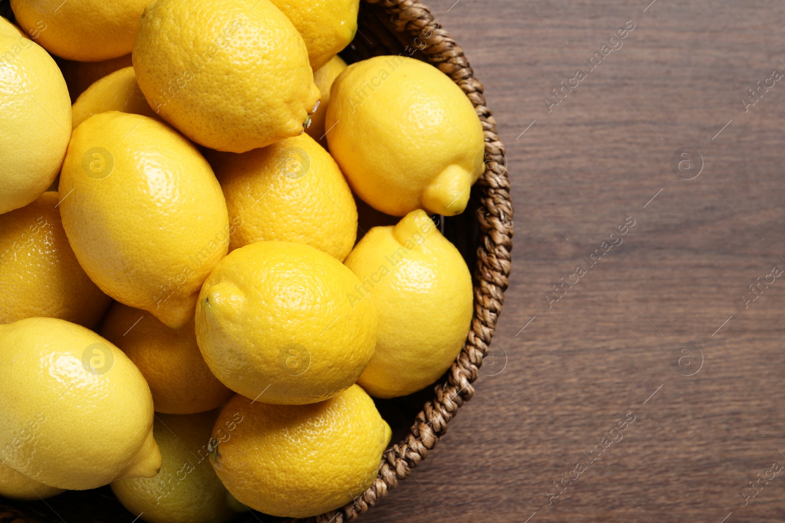 Photo of Fresh lemons in wicker basket on wooden table, top view. Space for text