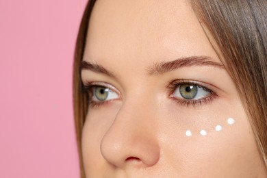 Photo of Young woman with cream around eye on pink background, closeup