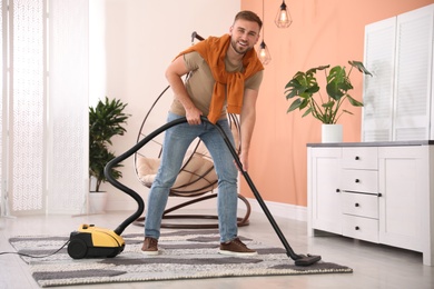 Photo of Young man cleaning carpet with vacuum cleaner at home