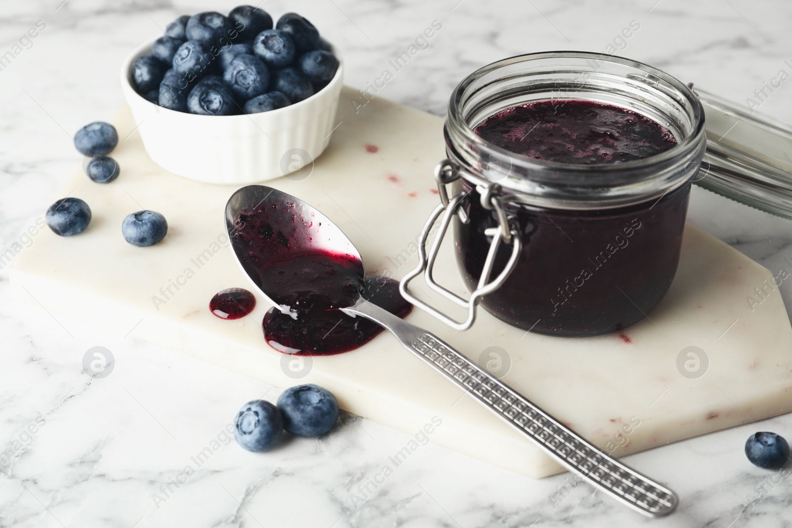 Photo of Jar of blueberry jam and fresh berries on white marble table