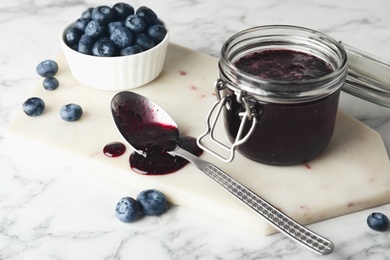 Photo of Jar of blueberry jam and fresh berries on white marble table