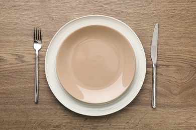 Clean plates, fork and knife on wooden table, top view