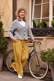 Beautiful senior woman standing near bicycle outdoors