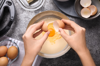 Woman preparing dough for Belgian waffles at grey table, top view