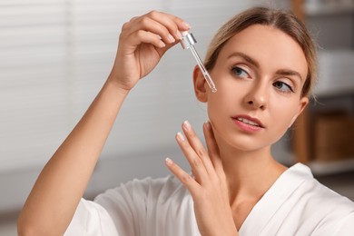 Photo of Beautiful woman applying cosmetic serum onto her face in bathroom