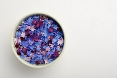 Beautiful colorful cornflowers petals in bowl on white table, top view. Space for text