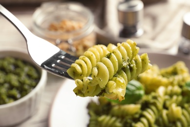 Photo of Fork with delicious basil pesto pasta over plate, closeup