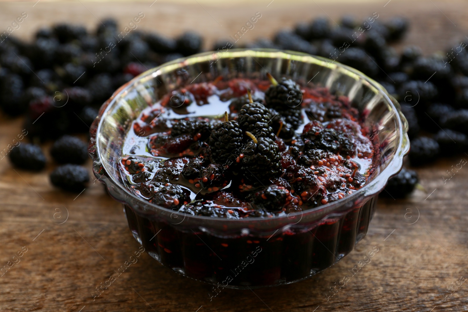 Photo of Bowl of sweet black mulberry jam on wooden table, closeup