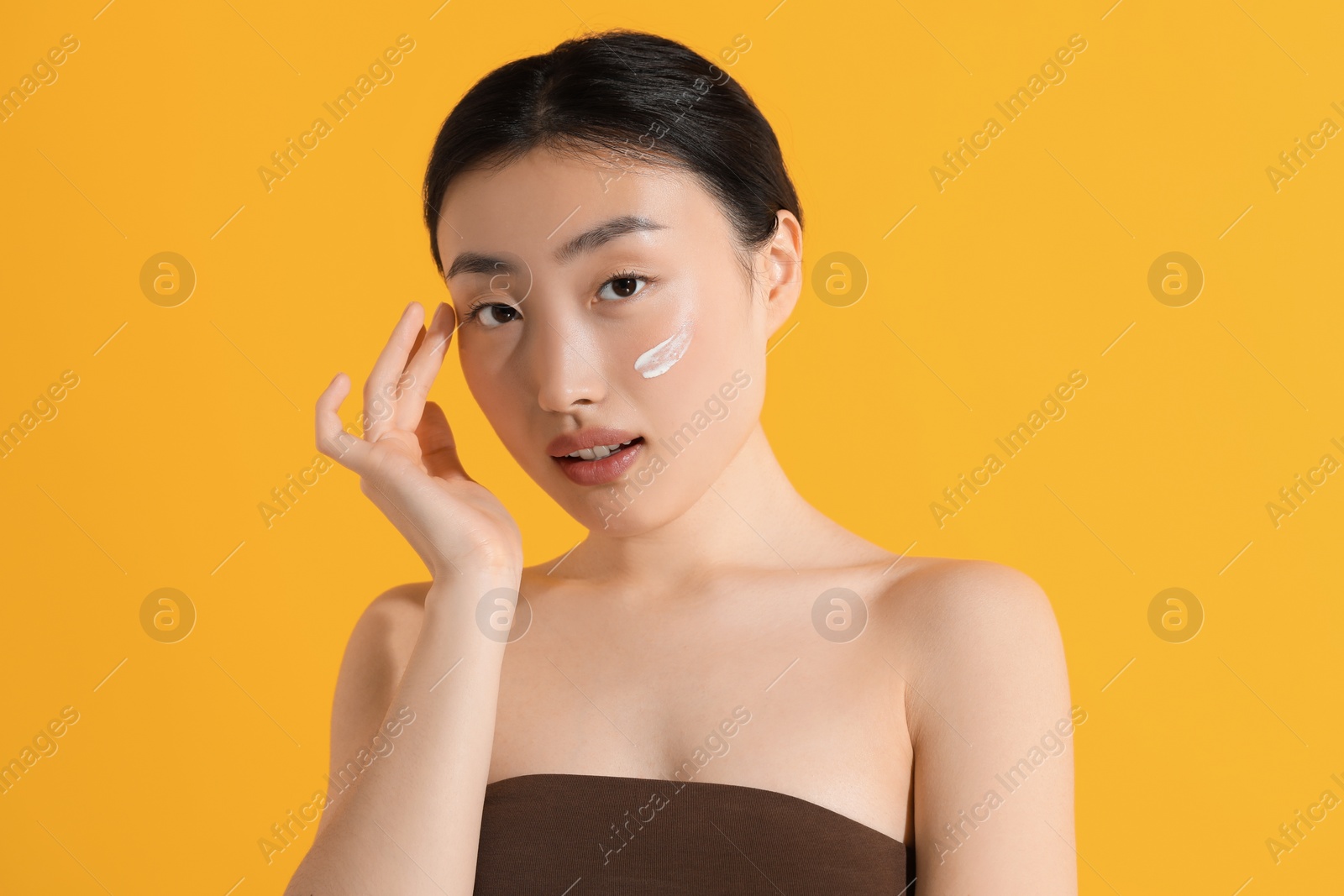 Photo of Beautiful young woman with sun protection cream on her face against orange background