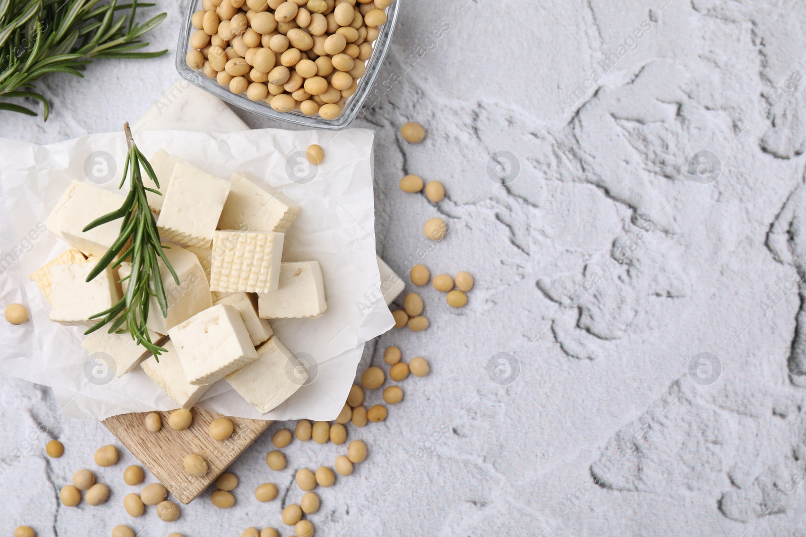 Photo of Delicious tofu cheese, rosemary and soybeans on light gray textured table, flat lay. Space for text
