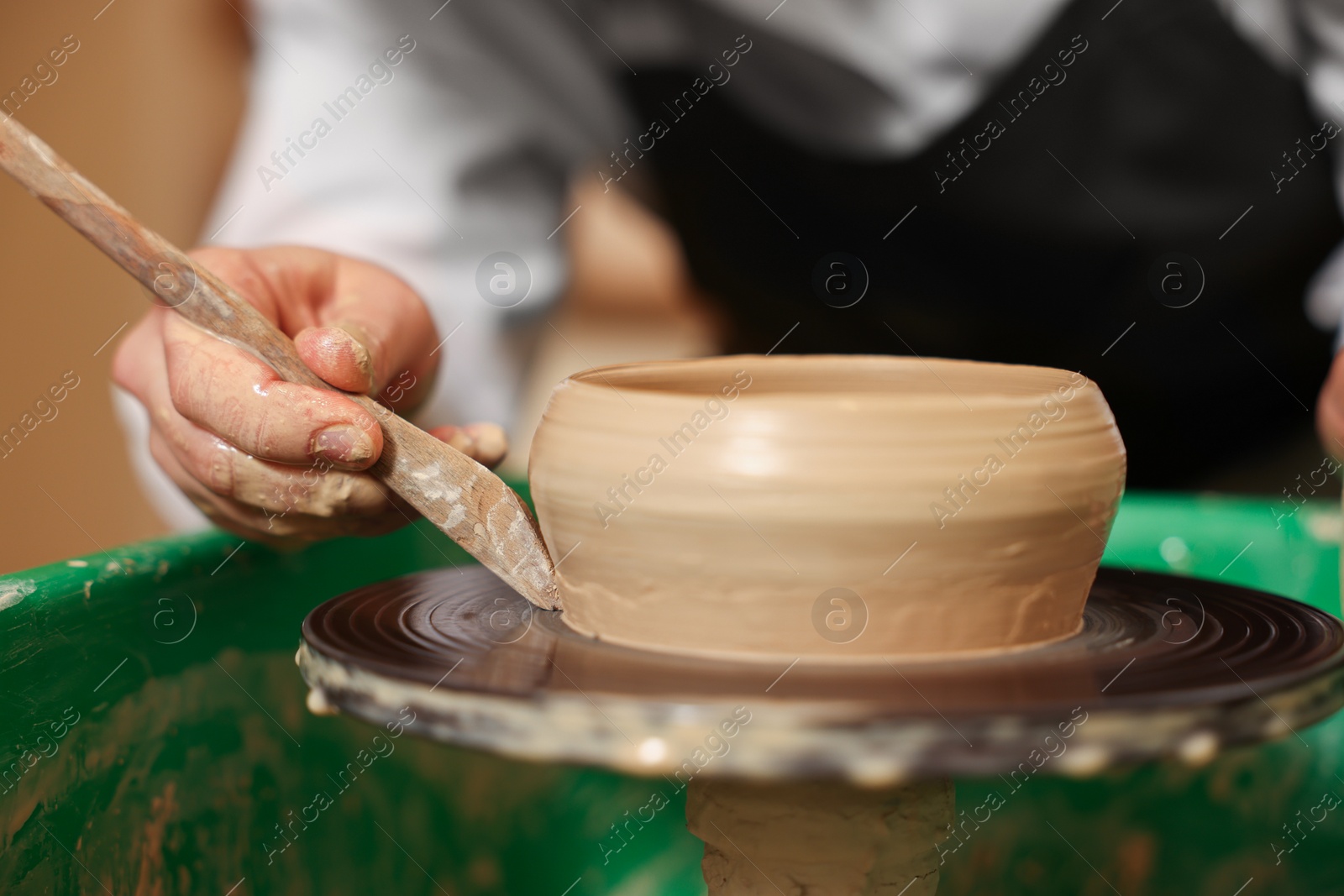 Photo of Clay crafting. Woman making bowl with modeling tool on potter's wheel, closeup