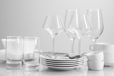 Photo of Set of many clean dishware, cutlery and glasses on light table
