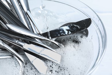 Photo of Pouring water into glass bowl with silverware in foam, closeup