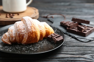 Photo of Plate of tasty croissant with powdered sugar and chocolate on dark wooden table. French pastry