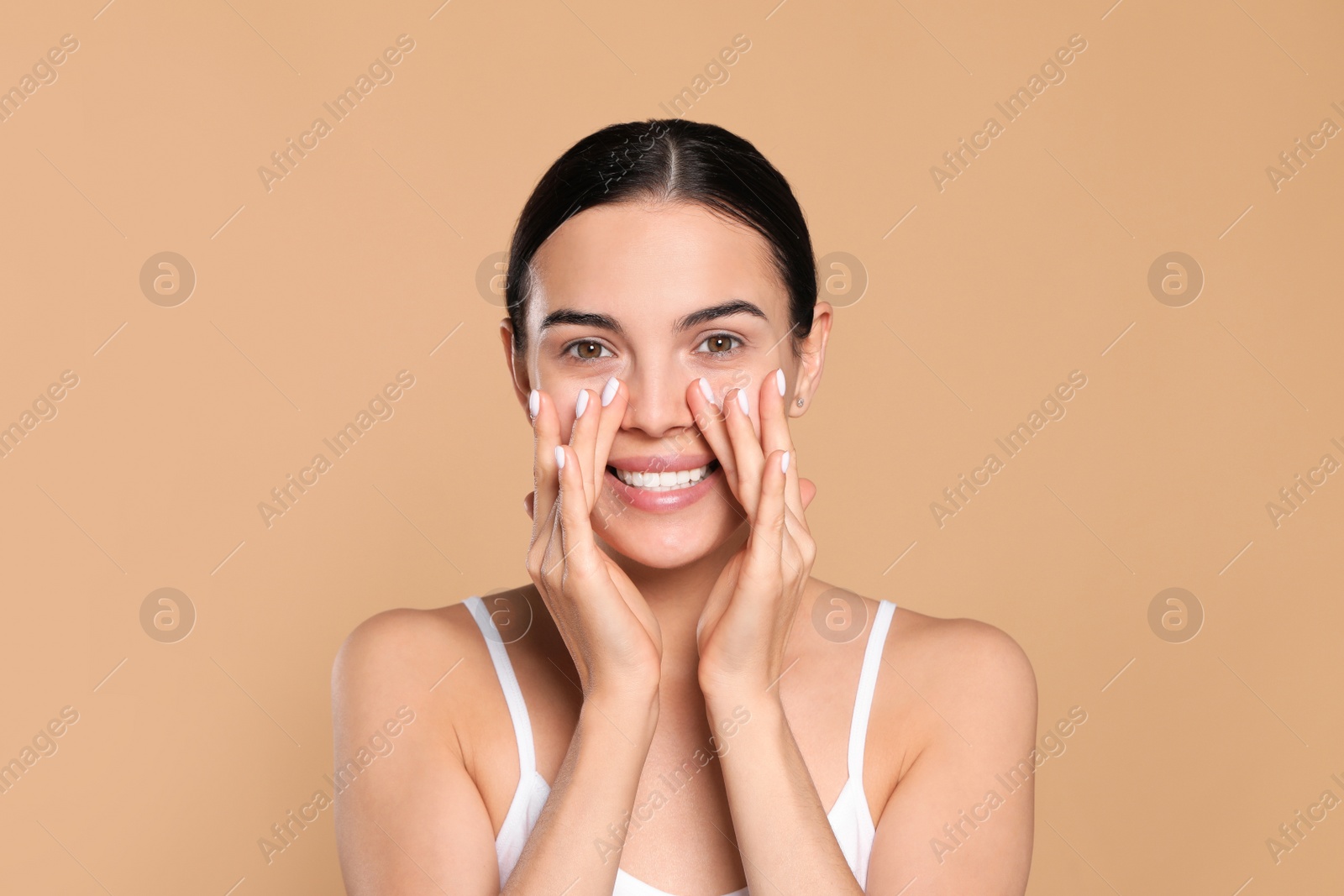 Photo of Beautiful young woman touching skin around eyes on beige background