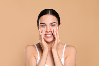 Beautiful young woman touching skin around eyes on beige background