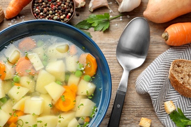 Bowl of fresh homemade vegetable soup with ingredients on wooden table, flat lay