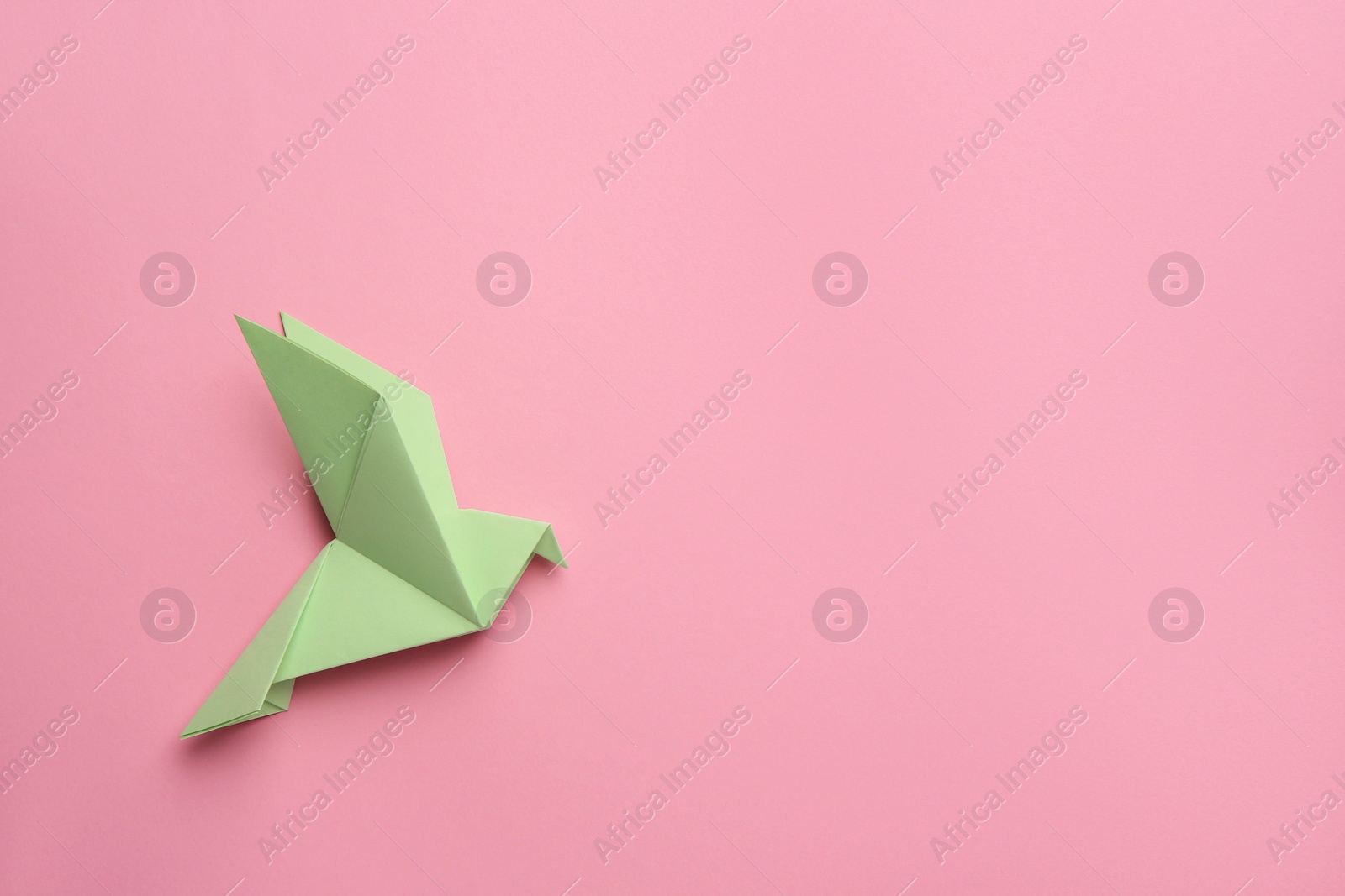 Photo of Beautiful light green origami bird on pink background, top view. Space for text