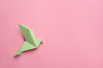 Photo of Beautiful light green origami bird on pink background, top view. Space for text