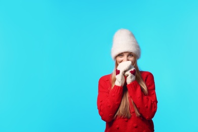 Portrait of emotional young woman in stylish hat, sweater and mittens on color background, space for text. Winter atmosphere