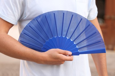 Photo of Man with blue hand fan outdoors, closeup