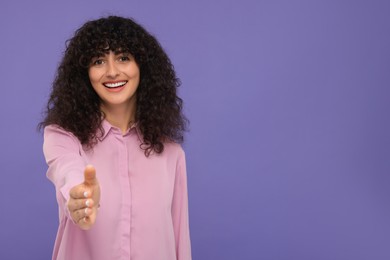 Happy young woman welcoming and offering handshake on violet background, space for text
