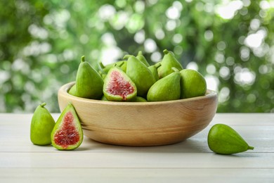 Cut and whole fresh green figs on white wooden table against blurred background