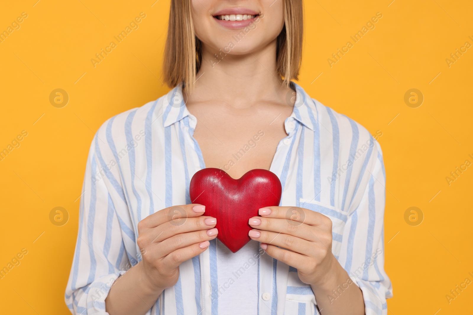 Photo of Young woman holding red heart on yellow background, closeup. Volunteer concept