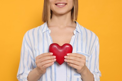 Young woman holding red heart on yellow background, closeup. Volunteer concept