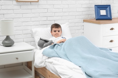 Photo of Cute child with stuffed bunny resting in bed at hospital