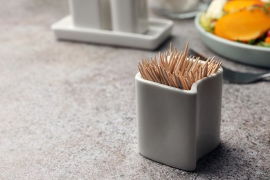 Holder with many bamboo toothpicks on grey table, closeup. Space for text