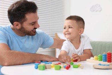 Photo of Motor skills development. Father and his son playing with colorful wooden pieces at table indoors