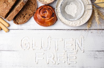 Photo of Many different products and phrase Gluten free written with flour on white wooden table, flat lay