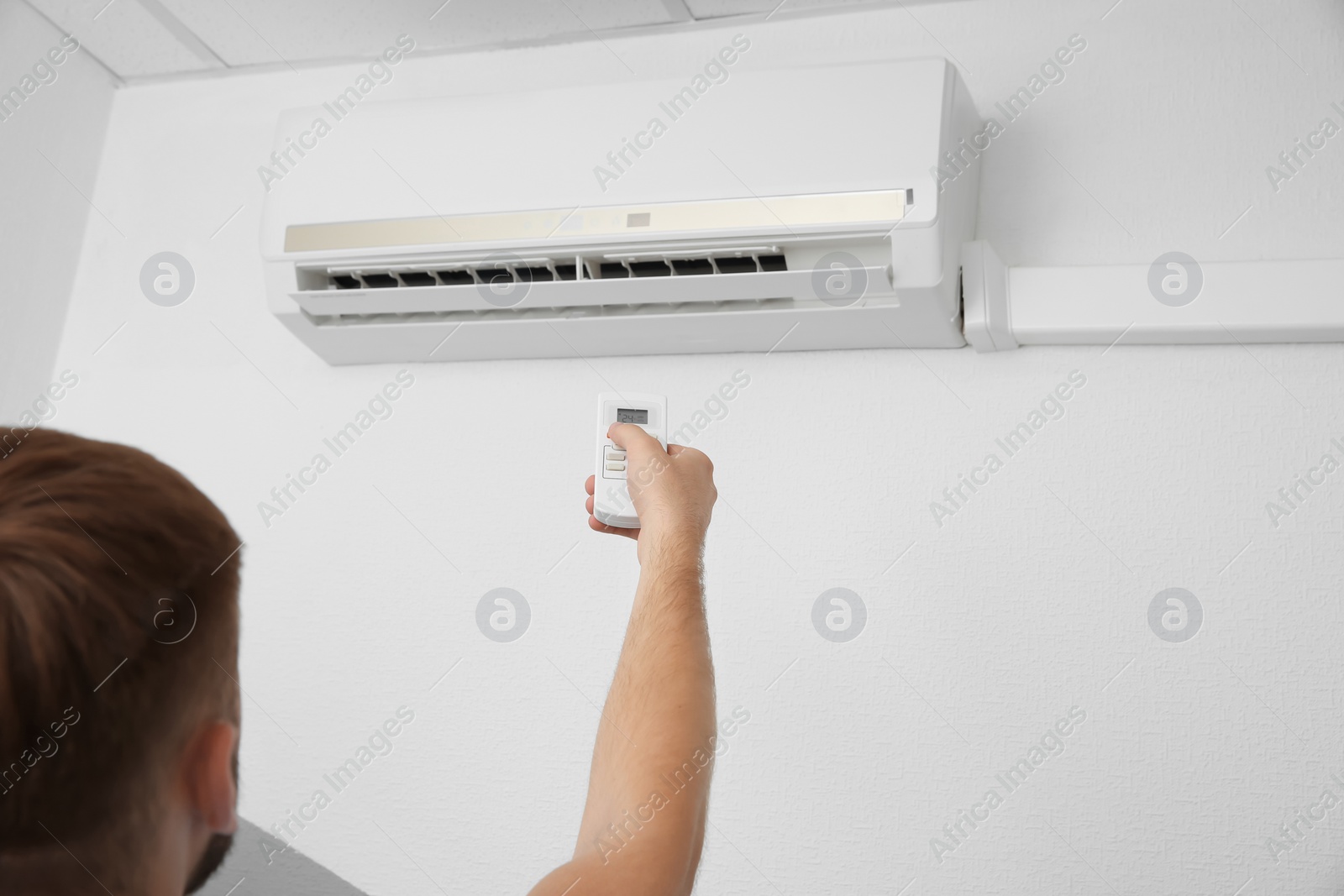 Photo of Man operating air conditioner with remote control indoors