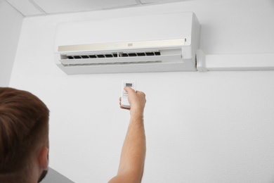 Man operating air conditioner with remote control indoors