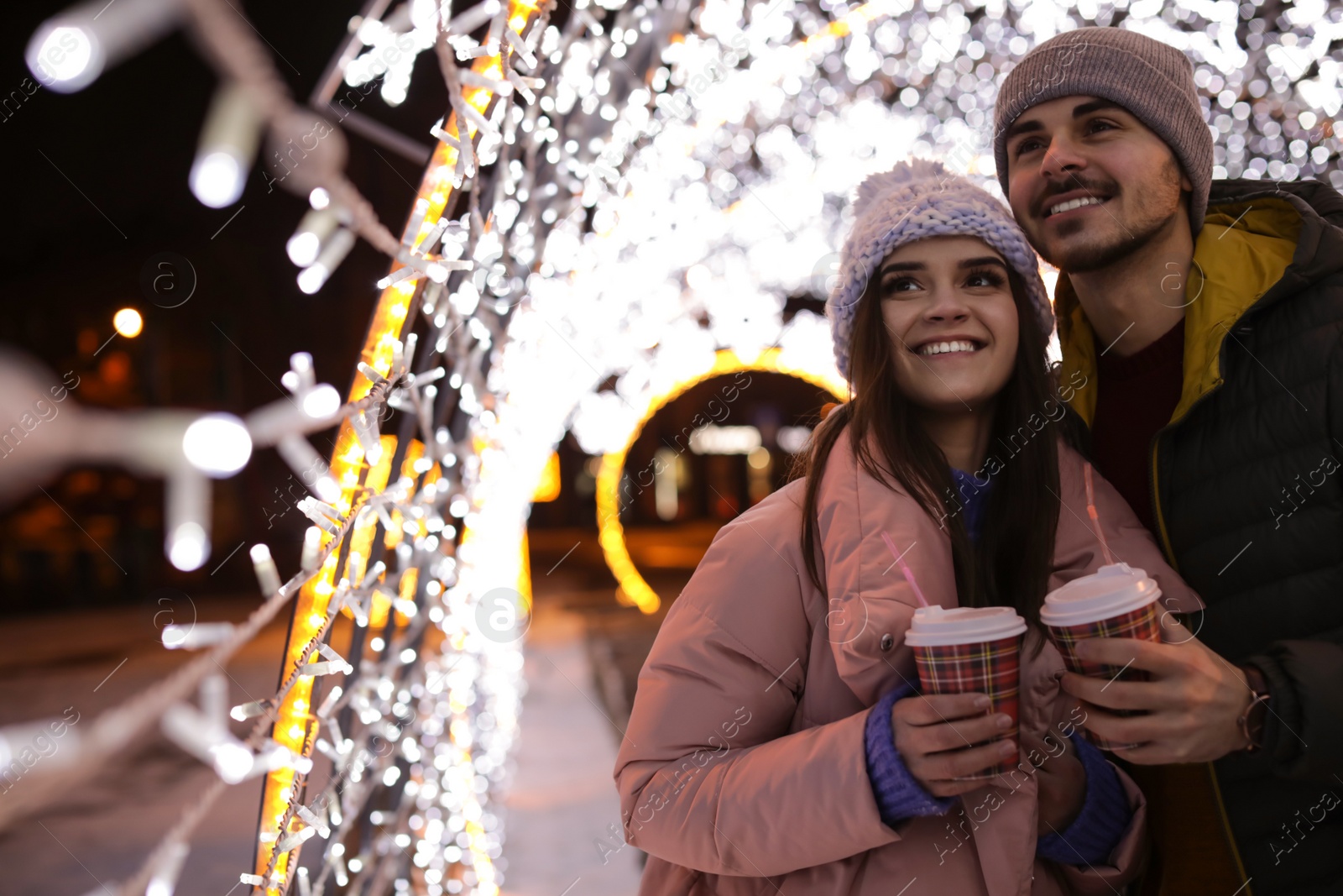 Photo of Young couple with cups of mulled wine at winter fair. Space for text