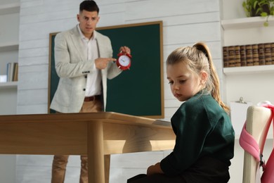 Photo of Teacher with alarm clock scolding pupil for being late in classroom
