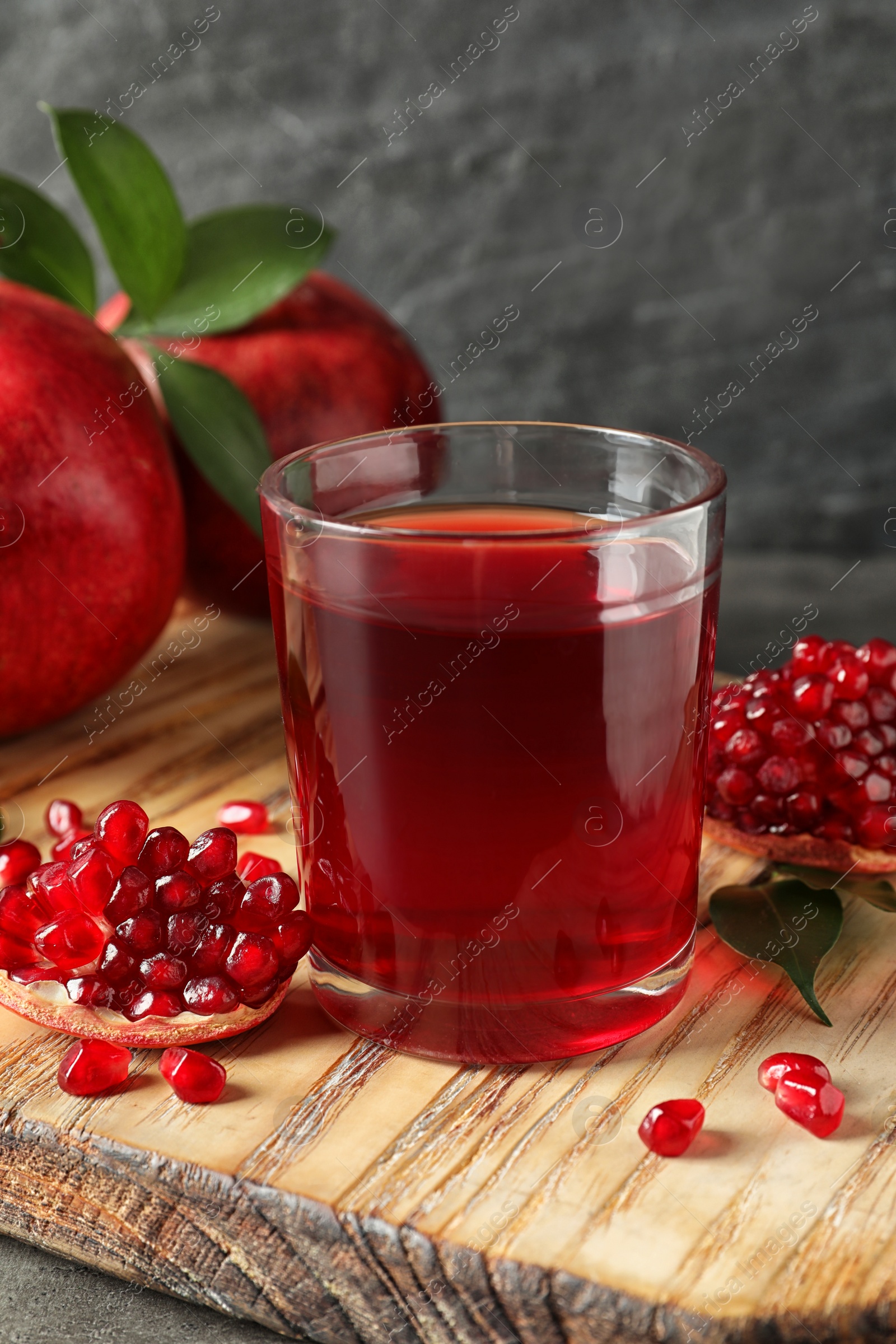 Photo of Glass of pomegranate juice and fresh fruits on wooden board against grey background