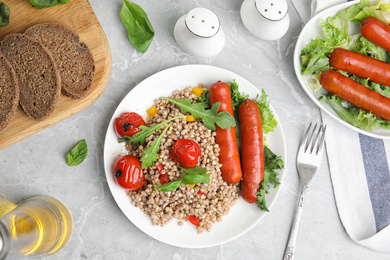 Photo of Tasty buckwheat porridge with sausages on light grey marble table, flat lay