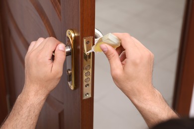 Repairman lubricating door lock indoors, closeup view