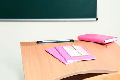 Photo of Wooden school desk with stationery near chalkboard in classroom