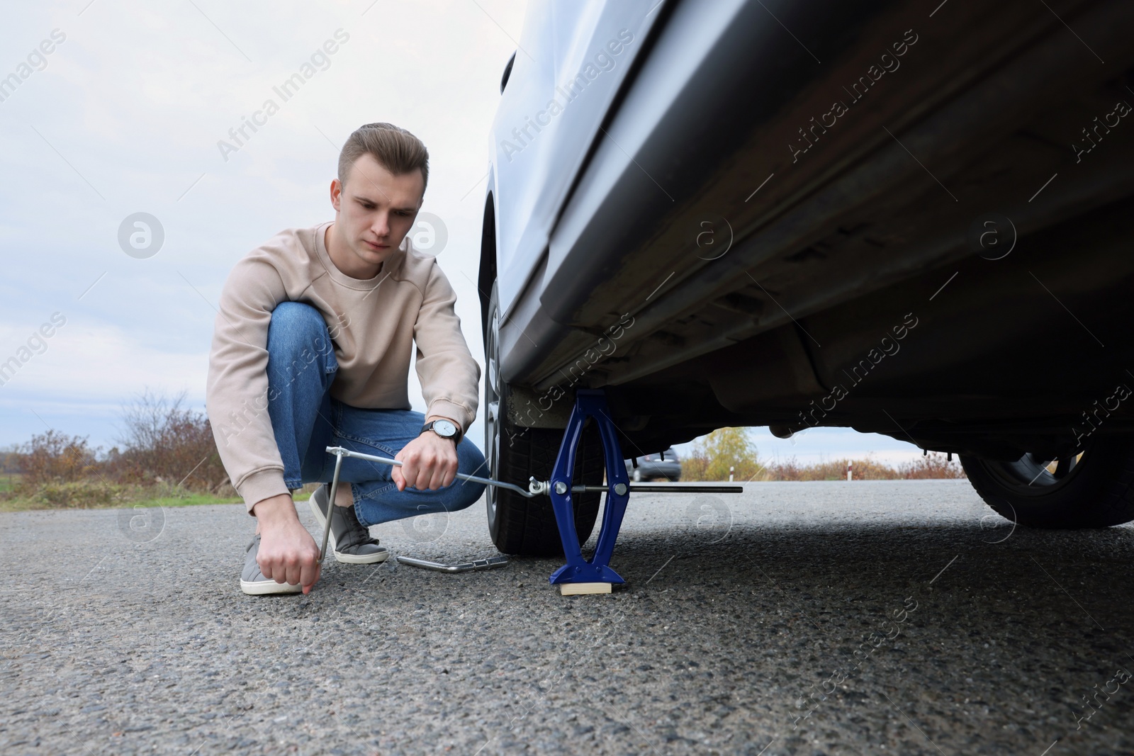 Photo of Young man changing tire of car on roadside