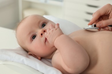 Photo of Pediatrician examining cute little baby with stethoscope in clinic, closeup