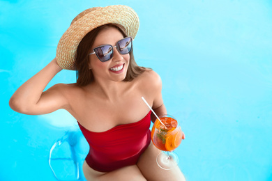 Photo of Woman with glass of refreshing drink in swimming pool