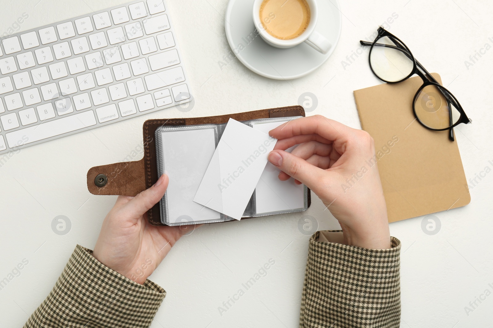 Photo of Woman holding leather business card holder with blank cards at white table, top view