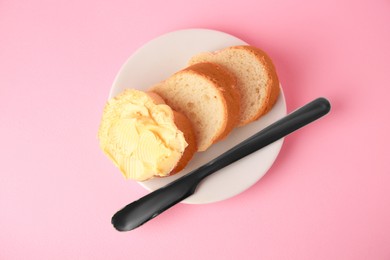 Photo of Slices of delicious baguette with butter and knife on pale pink background, top view