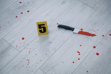 Knife in blood near crime scene marker on wooden floor