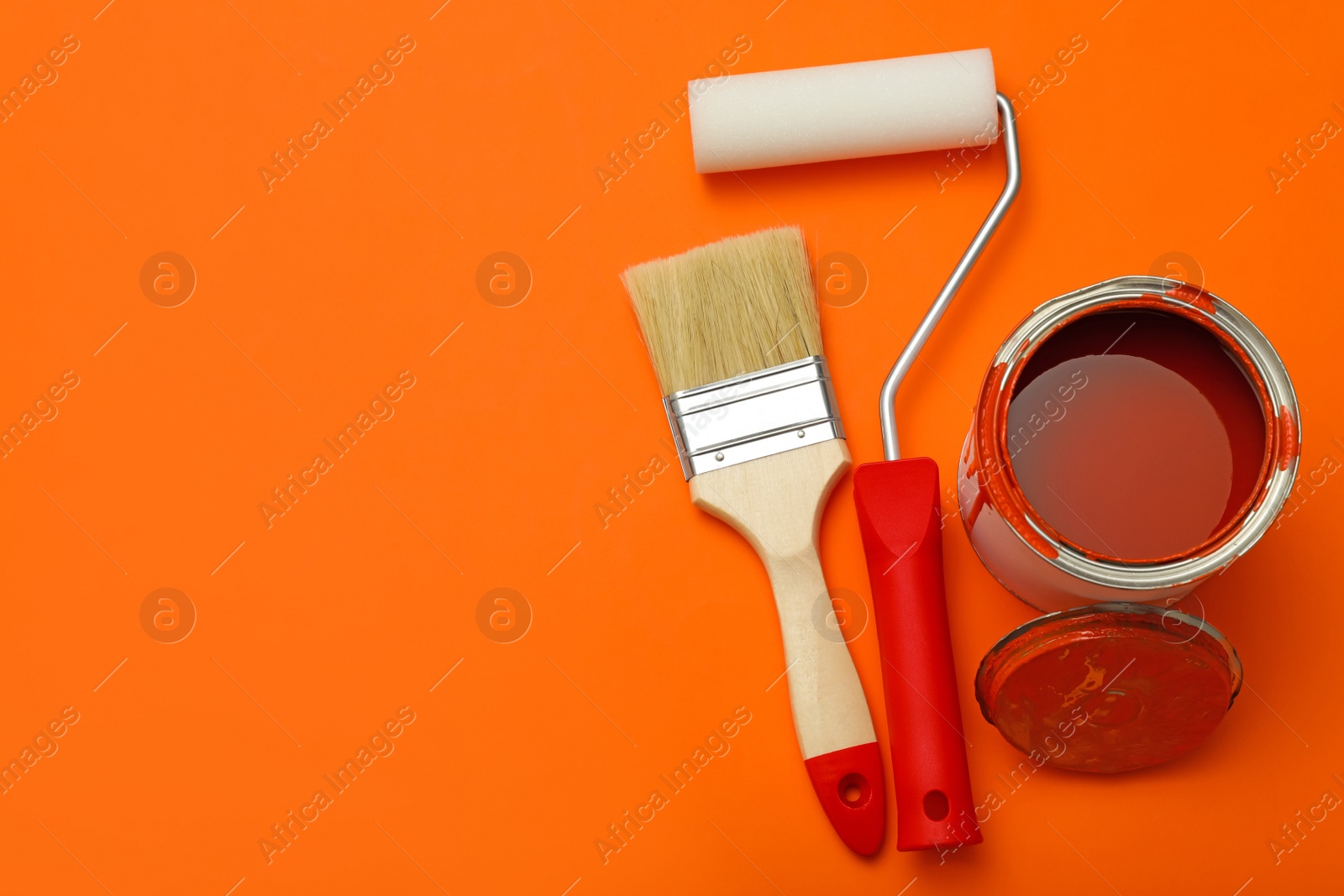 Photo of Can of orange paint, brush and roller on color background, flat lay. Space for text
